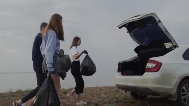 Les jeunes volontaires mettent des sacs poubelles dans la voiture. Pollution plastique et concept de problème environnemental. Nettoyage volontaire de la nature du plastique. — Video