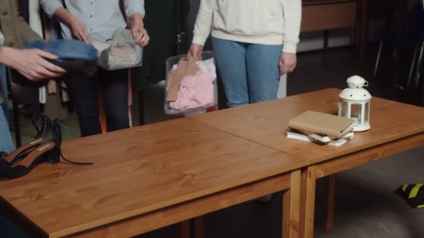女性のクローズアップは、古着屋でテーブルの上に服を置いた箱を置く — ストック動画