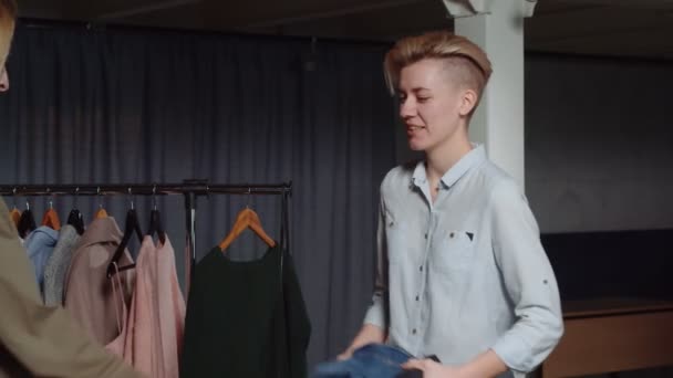 Uma mulher vendedor dá roupas para outra mulher cliente em segunda mão loja de roupas — Vídeo de Stock