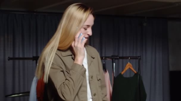 Genç kadın satıcı telefonla konuşuyor ve ikinci el giyim mağazasında çalışıyor. — Stok video