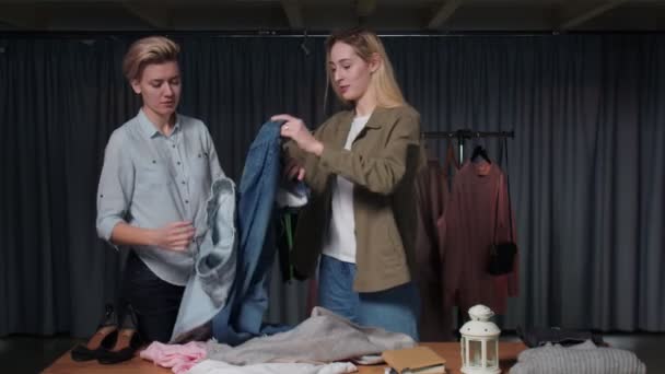 Genç kadınlar ikinci el dükkanında çalışanlar masadaki kıyafetleri düzenler. — Stok video