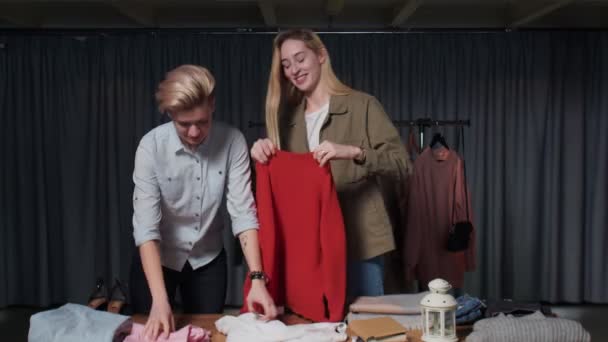 Jovens mulheres trabalhadores da loja de segunda mão classificar roupas na mesa — Vídeo de Stock
