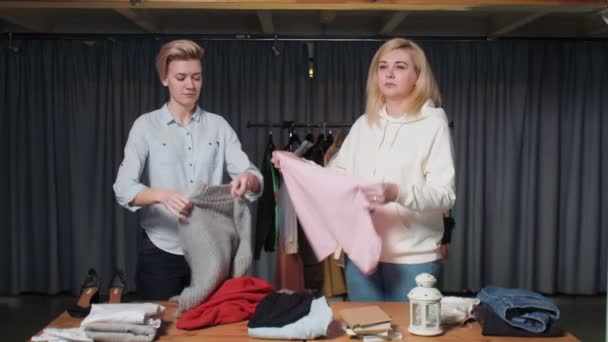 Νεαρές γυναίκες Εργάτες μεταχειρισμένων καταστημάτων ταξινομήσετε τα ρούχα στο τραπέζι — Αρχείο Βίντεο