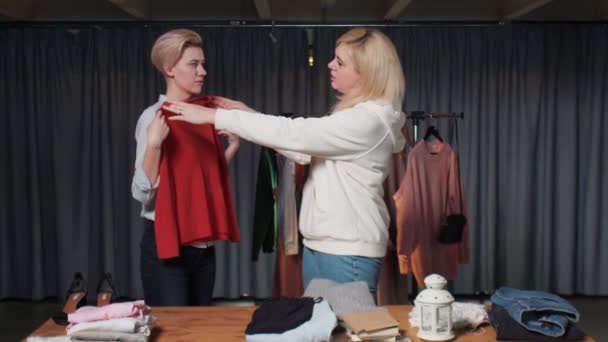 Genç bir kadın ikinci el giyim mağazasında kırmızı bir kazak deniyor. — Stok video