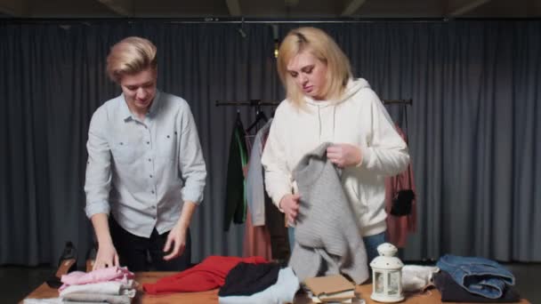 若い女性中古店の労働者はテーブルの上に服をソート — ストック動画