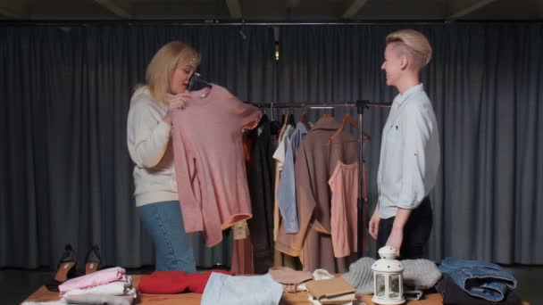 Las mujeres jóvenes se prueban un suéter rosa en la tienda de ropa de segunda mano — Vídeos de Stock