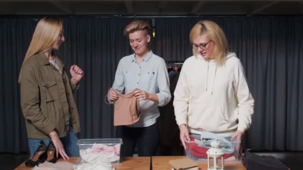 Három nő használt bolti munkások válogatás ruhák az asztalon — Stock videók