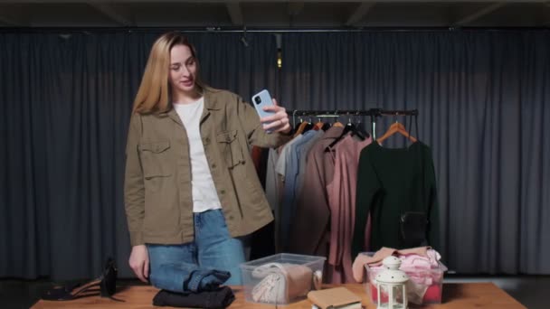 Joven vendedora registra historias de ropa en su teléfono en tienda de ropa de segunda mano — Vídeos de Stock