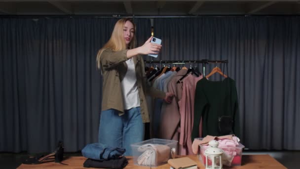 Jovem vendedora registra histórias de roupas em seu telefone na loja de roupas de segunda mão — Vídeo de Stock