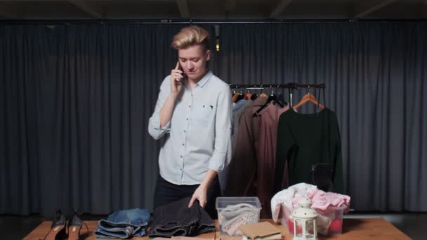 Девушка-продавец разговаривает по телефону и работает в магазине подержанной одежды — стоковое видео