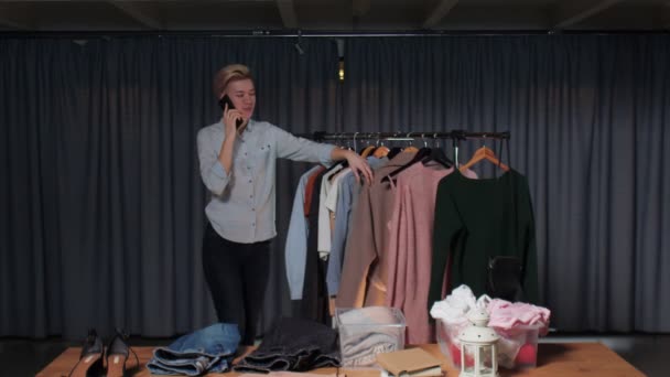 Jonge vrouw verkoper praat met de klant via de telefoon en werkt in tweedehands kleding winkel — Stockvideo