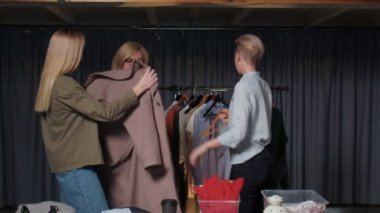 Genç bir kadın ikinci el giysi dükkanında pembe bir ceket deniyor.