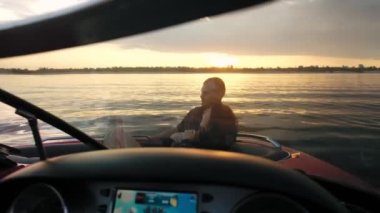 Bir adamla bir kız motorlu teknede oturmuş gün batımını seyrediyorlar. Romantik atmosfer.