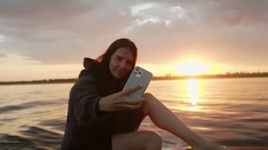 Bir kadın gün batımında motorlu bir teknede kendi fotoğrafını çekiyor.