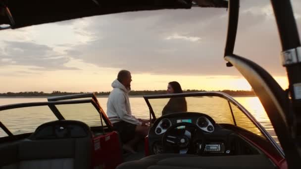 Um tipo e uma rapariga estão sentados num barco a motor a ver o pôr-do-sol. Ambiente romântico. — Vídeo de Stock