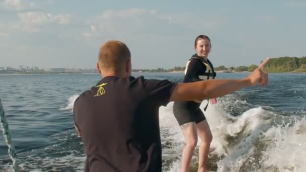 A rapariga é surfista, anda de wakeboard. Um wakeboarder experiente ajuda uma menina — Vídeo de Stock