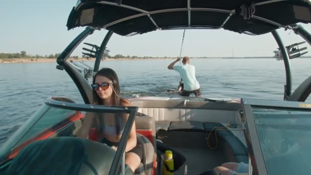 Μια γυναίκα οδηγεί ένα μηχανοκίνητο σκάφος, και στο βάθος ένας τύπος είναι καβάλα σε ένα wakeboard, και ο άνθρωπος τον βοηθά — Αρχείο Βίντεο