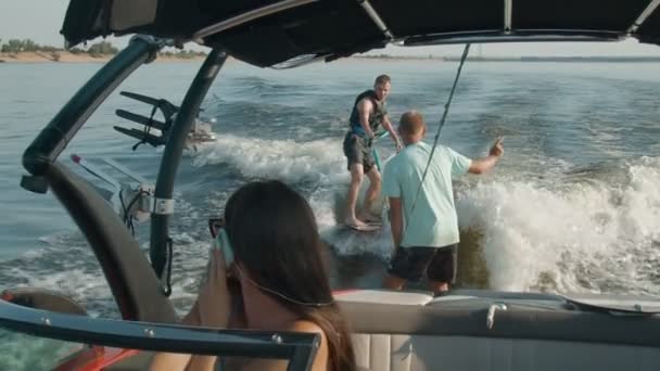 Una donna sta guidando una barca a motore, e sullo sfondo un ragazzo sta guidando un wakeboard, e l'uomo lo sta aiutando — Video Stock