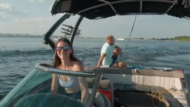 Uma mulher está dirigindo um barco a motor, e um homem está sentado no fundo e desfrutando do ar fresco agradável — Vídeo de Stock