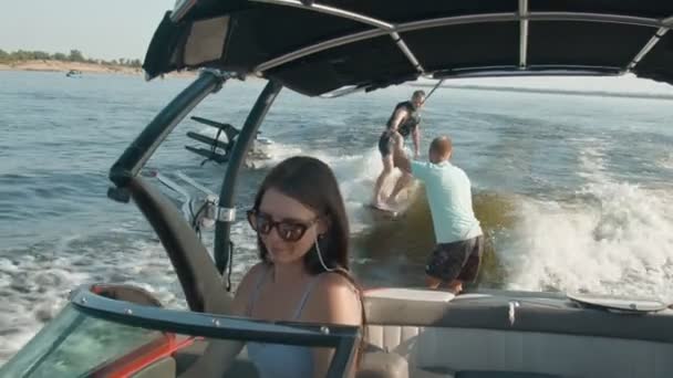 女性がモーターボートを運転していて、後ろに男がウェイクボードに乗っていて、男は彼を助けている — ストック動画