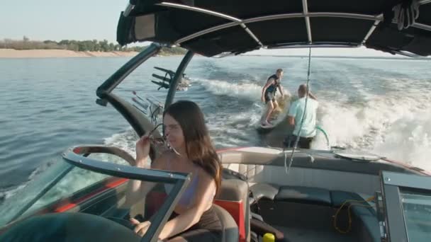 Bir kadın motorlu tekne kullanıyor, ve arka planda bir adam wakeboard kullanıyor, ve erkek ona yardım ediyor. — Stok video