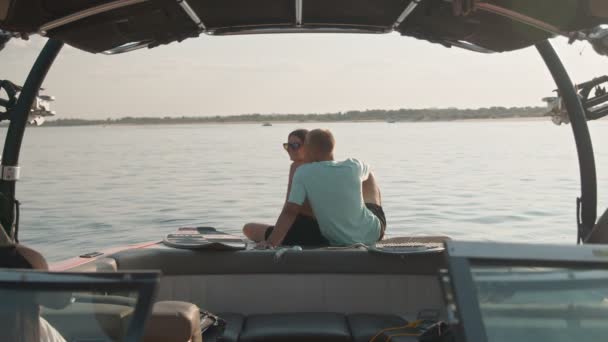 A guy and a girl are sitting in a motor boat, talking and looking into the distance. Romantic atmosphere. — Stock Video