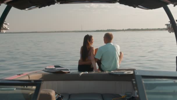 A guy and a girl are sitting in a motor boat, talking and looking into the distance. Romantic atmosphere. — Stock Video