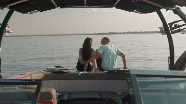 Un ragazzo e una ragazza sono seduti in una barca a motore, baciare e guardare in lontananza. Atmosfera romantica. — Video Stock