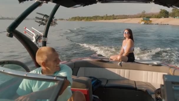 Um homem dirige um barco a motor, e uma mulher no fundo se senta e desfruta do clima agradável — Vídeo de Stock