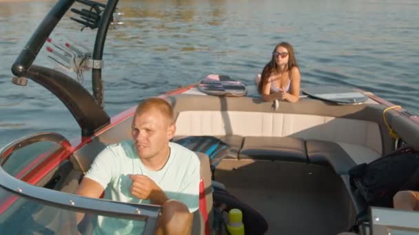 Un homme conduit un bateau à moteur, et une femme en arrière-plan est allongée sur le ventre et profite du beau temps — Video