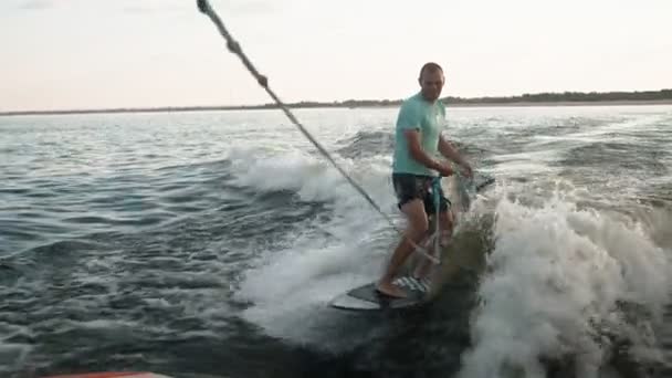 Un surfista saltando sobre un wakeboard. Un experimentado wakeboarder rocía agua en la cámara. — Vídeos de Stock