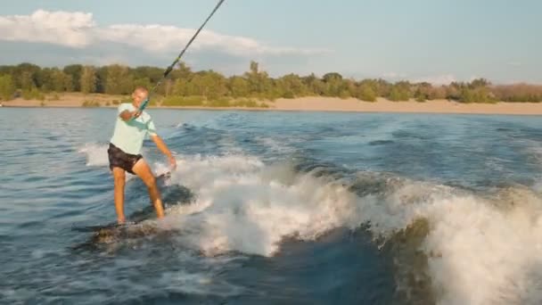 Een surfer springt op een wakeboard. Een ervaren wakeboarder spuit waterdruppels in de camera. — Stockvideo