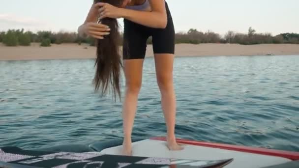 Une femme se tient debout sur un bateau à moteur et recueille ses cheveux dans une queue de cheval — Video