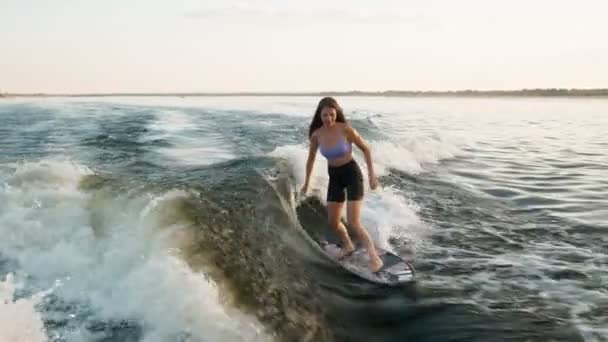 Samica surfera skacząca na desce. Doświadczony wakeboarder chlapie krople wody do kamery. — Wideo stockowe