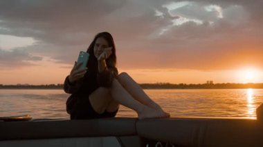 Bir kadın gün batımında motorlu bir teknede kendi fotoğrafını çekiyor.