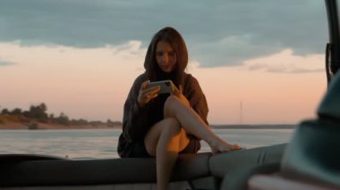 Bir kadın gün batımında motorlu bir teknede telefonda oturuyor.