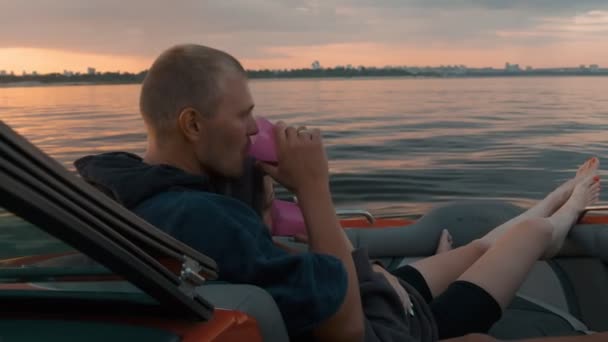 En kille och en flicka kramas sött vid solnedgången sitter i en båt — Stockvideo