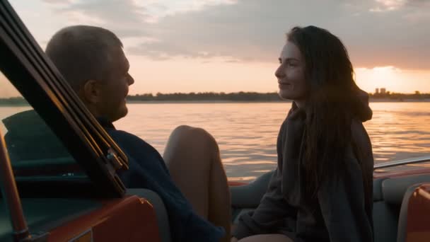 Um cara e uma menina abraçar bonito ao pôr do sol sentado em um barco — Vídeo de Stock
