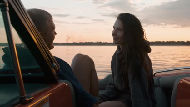 Um cara e uma menina abraçar bonito ao pôr do sol sentado em um barco — Vídeo de Stock