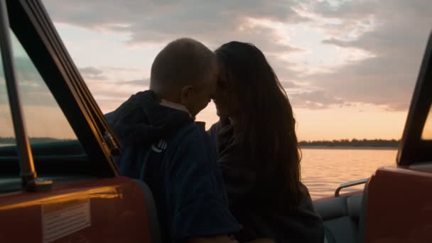 A guy and a girl are sitting in a motor boat kissing and watching the sunset. Romantic atmosphere. — Stock Video