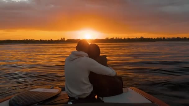 A guy and a girl are sitting in a motor boat and watching the sunset. Romantic atmosphere. — Stock Video