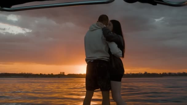 A guy and a girl are standing and cuddling sweetly in a motor boat and looking at the sunset. Romantic atmosphere. — Stock Video