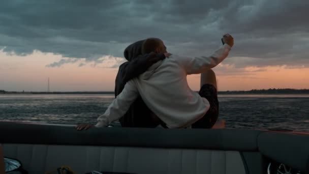 Мужчина и женщина сидят на моторной лодке и фотографируют на закате — стоковое видео
