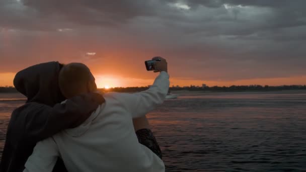 Um homem e uma mulher sentam-se num barco a motor e tiram fotos ao pôr-do-sol — Vídeo de Stock