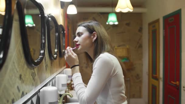 Boční pohled na ženu používající rtěnku na make-up před zrcadlem, šťastná žena používající kosmetiku pro krásu — Stock video