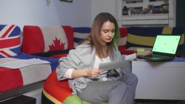 Finansal belgeleri elinde tutan genç bir kadın, internet bankacılığı için dizüstü bilgisayar kullanıyor, faturaları ödüyor dizüstü bilgisayarda çalışıyor, belgeleri işliyor, yeşil ekran üzerinde çalışıyor.