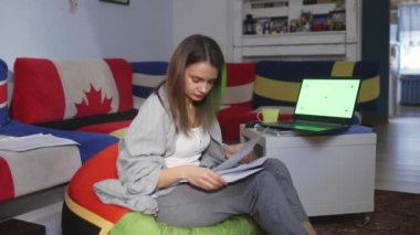 Finansal belgeleri elinde tutan genç bir kadın, internet bankacılığı için dizüstü bilgisayar kullanıyor, faturaları ödüyor dizüstü bilgisayarda çalışıyor, belgeleri işliyor, yeşil ekran üzerinde çalışıyor.
