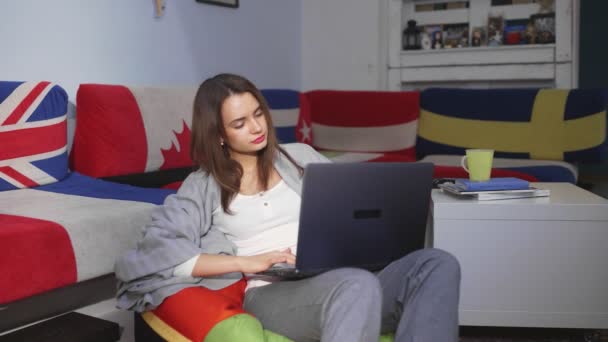 Eine junge Frau sitzt in einem Raum an einem Computer und blättert durch einen Nachrichtenfeed. Freizeit. — Stockvideo
