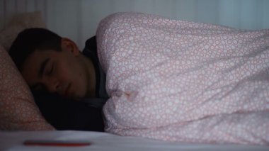 Genç bir adam yatakta uyuyor, gece telefonla bir mesaj alıyor..
