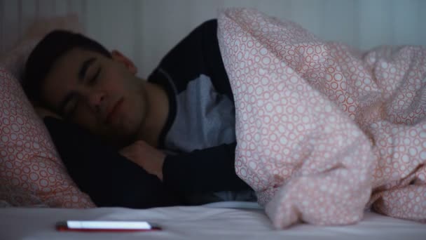 Un giovanotto dorme a letto, riceve un messaggio al telefono di notte. — Video Stock